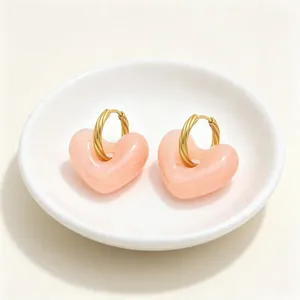 Detailweergave van retro roze hars hart oorbellen met gedraaide goudkleurige ringen