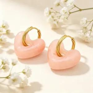 Detailweergave van roze gemarmerde hartsieraden met gouden gedraaide stalen hoepeloorbellen.