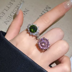 Detailaufnahme eines funkelnden grünen Blumenrings und eines rosa Zirkonrings am Finger