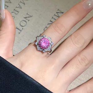 Makro-Detail eines eleganten Rings mit rosa Zirkon-Blüte und weißen Steinen am Finger