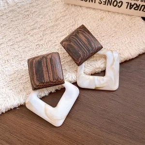 Close-up of retro geometric stud earrings with wooden squares and marbled acrylic pendants.