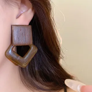 Detail close-up of vintage geometric earrings featuring a wood top and amber acrylic pendant