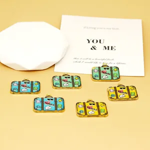 Macro view of colorful enamel suitcase charms with TRAVEL print and travel icons for DIY jewelry.