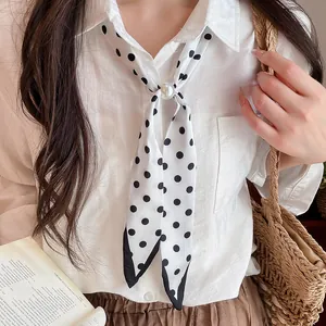 Detailansicht eines stilvollen weißen Polka-Dot-Seidenschals mit Perle auf weißem Hemd.
