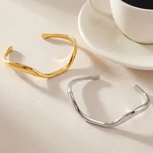Close-up of minimalist wave-shaped stainless steel cuff bracelets in gold and silver