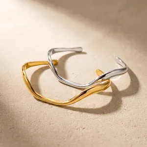 Close-up of elegant gold and silver irregular wavy line stainless steel bangles on sand