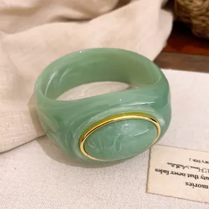 Detailansicht eines grünen Acryl-Armreifs mit Marmoreffekt und einer goldfarbenen Metalleinfassung.