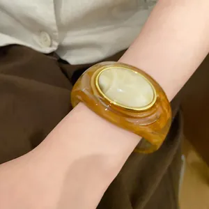 Nahaufnahme eines bernsteinfarbenen Acryl-Armreifs mit marmoriertem Stein am Handgelenk