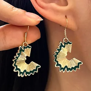 Detail view of creative 3D gold pencil shaving earrings with green enamel accent.
