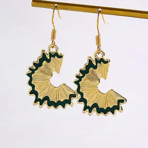 Detailed close-up of creative gold pencil shaving earrings with dark green enamel.