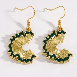 Detailed view of creative gold pencil shaving earrings featuring dark green enamel accents