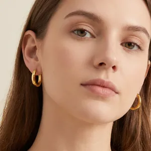 Close-up detail of a female model wearing polished gold stainless steel hoop earrings.
