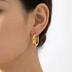 Close-up view of a minimalist gold stainless steel hoop earring on a female model's ear.