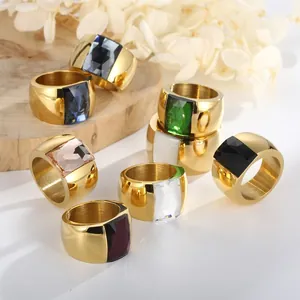 Wide gold titanium steel rings with various faceted colorful crystals on wood background