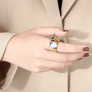 Close-up of a wide gold stainless steel ring featuring a large faceted glass stone on a hand.
