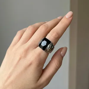 Close-up detail of a wide titanium steel ring with a faceted black stone worn on a hand