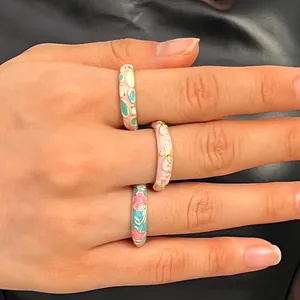 Detailed view of three colorful floral enamel rings worn on fingers with a black background.