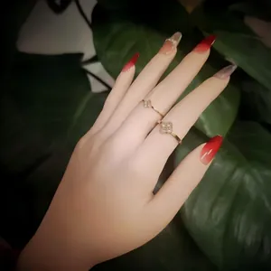 Detail view of two gold four-leaf clover rings with crystals worn on a manicured hand.