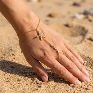 Detailansicht der goldenen Seestern-Handschmuckkette mit Zirkonia auf Sandhintergrund.