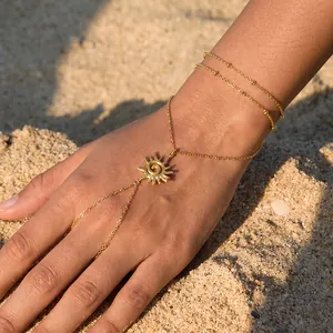 Nahaufnahme einer Handkette aus goldfarbenem Edelstahl mit Sonnenanhänger auf Sandhintergrund