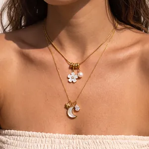 Primer plano de collares de acero dorado con colgantes de flores, luna y perlas.