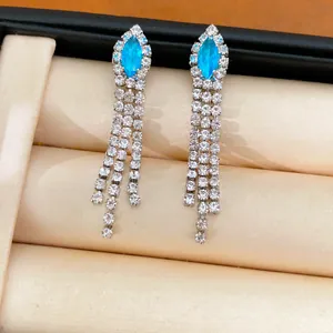 Vue détaillée des boucles d'oreilles à pompons dorées avec pierres bleues claires