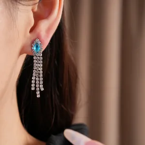 Gros plan d'une boucle d'oreille pompon en zircon plaqué or 14k avec pierre bleue.