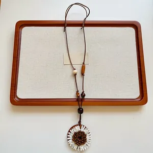 Vista dettagliata di una collana lunga con ciondolo a forma di girasole in tessuto bianco.