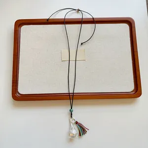 Dettaglio di pendente geometrico argento con nappa colorata su cordino nero
