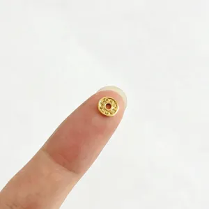 Vue macro d'une minuscule perle intercalaire en acier doré 18K sur le bout d'un doigt