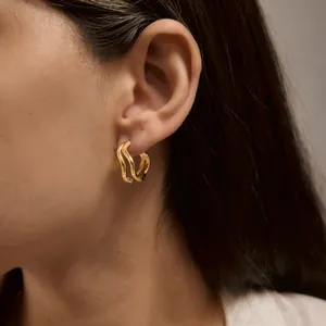 Détail rapproché des boucles d'oreilles vagues doubles en acier inoxydable doré