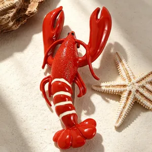 Detail shot of a vibrant red enamel lobster brooch on a beach-themed background.