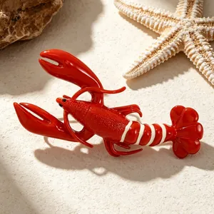 Macro detail view of a vibrant red lobster brooch resting on a beach-themed sandy background
