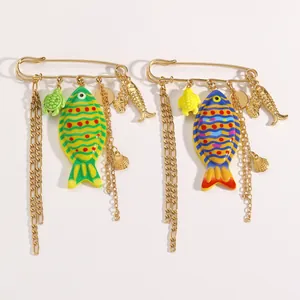Close-up of gold-tone safety pin brooches with colorful fish and turtle charms.