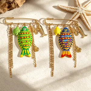 Macro detail of colorful fish-shaped brooches with golden chains on beach background