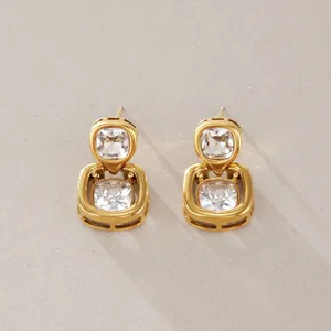 Detailgetreue Makroansicht goldener Titanstahl-Ohrringe mit funkelnden quadratischen Steinen.
