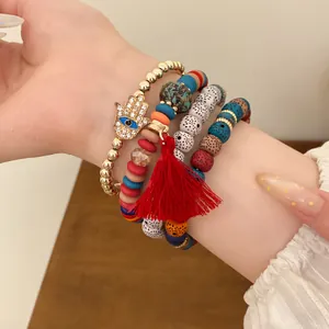 Close-up detail of bohemian beaded bracelet set featuring Hamsa hand charm and red tassel