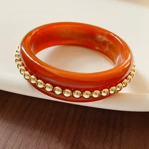Detail of an orange resin bangle accented with small gold spheres on white tray