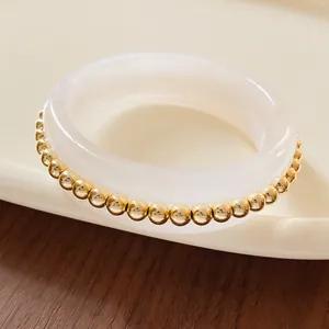 Close-up of a minimalist white resin bangle accented with polished golden metal beads