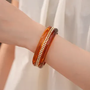 Close-up of elegant amber resin bangles and crystal studded bracelet on a wrist