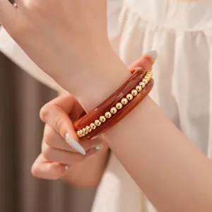 Detail view of a luxury amber resin bangle featuring inlaid gold beads on a model's wrist