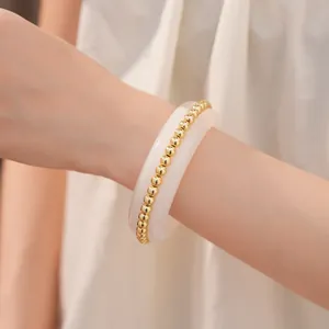 Close-up of a minimalist white resin bangle inlaid with elegant golden beads on a wrist