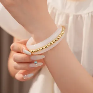 Detailed macro shot of elegant gold beads embedded in a smooth white resin bangle bracelet.
