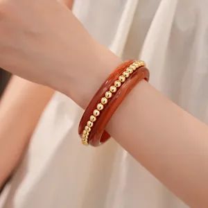 Close-up of a layered bangle set featuring reddish-brown resin and gold beads.