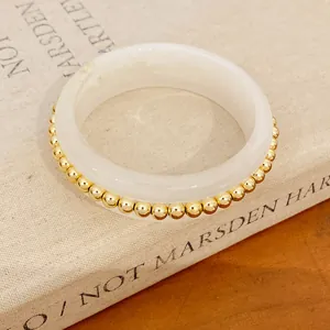 Detailed macro shot of a white resin bangle with gold-colored bead accents on a vintage book.