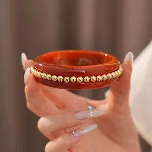Close-up view of red resin bangle featuring gold beads held by a hand with stylish nails.