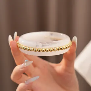 Detailed shot of a cream resin bangle with elegant gold bead trimming held by hand
