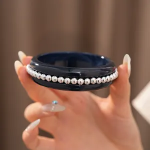 Detail view of navy blue resin bangle with silver bead embellishments held by hand