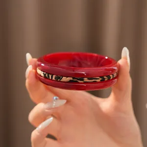 Close-up detail of a red resin bangle with a striking leopard print band held by hand