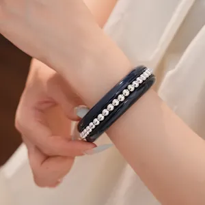 Close-up of glossy dark resin bangle and silver bead bracelet set on wrist